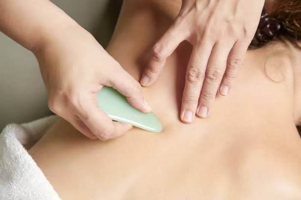 Gua Sha-style body treatment using a jade tool on a client's back.